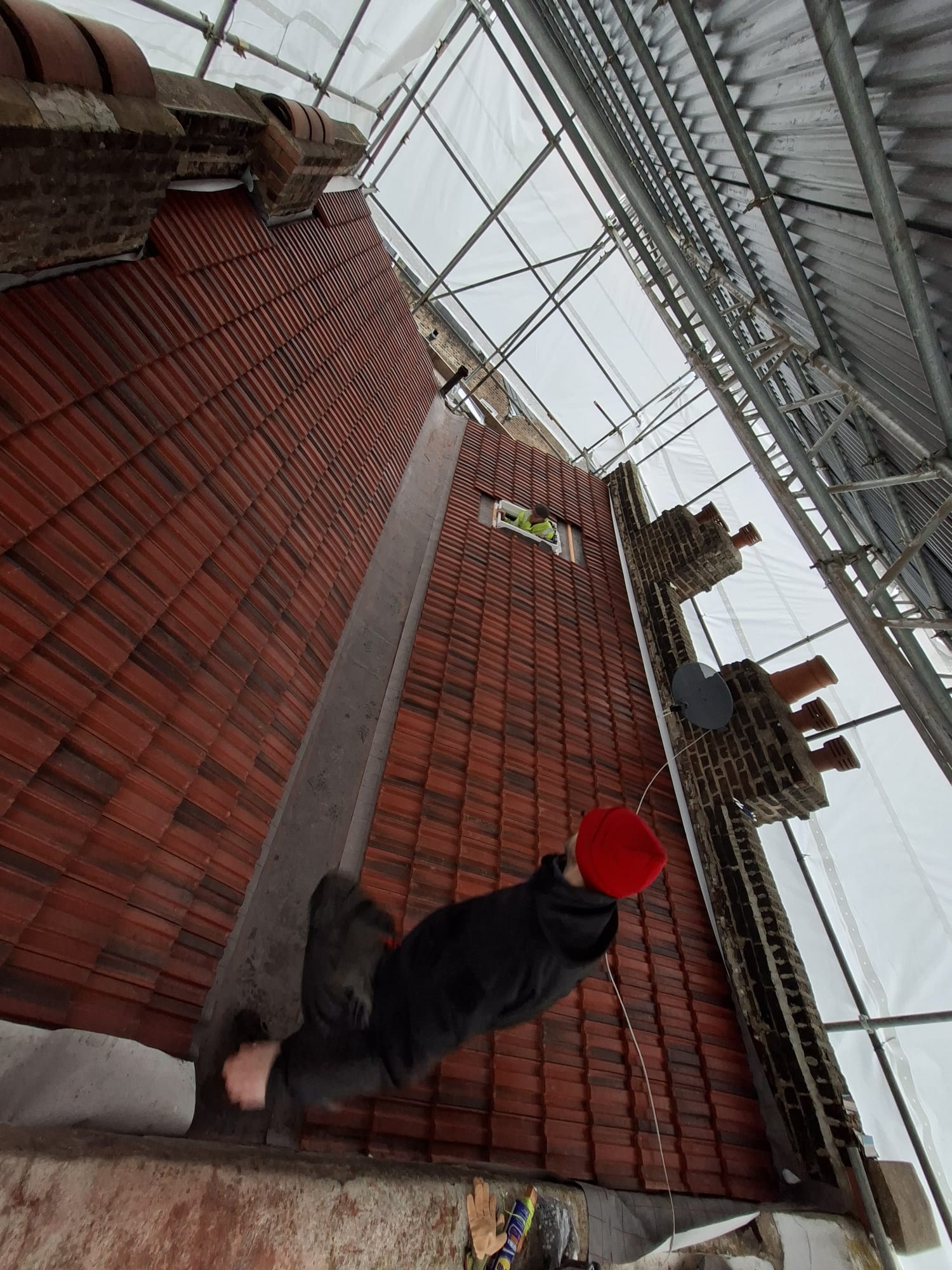 Roofer tiling a new roof on scaffolding during replacement project