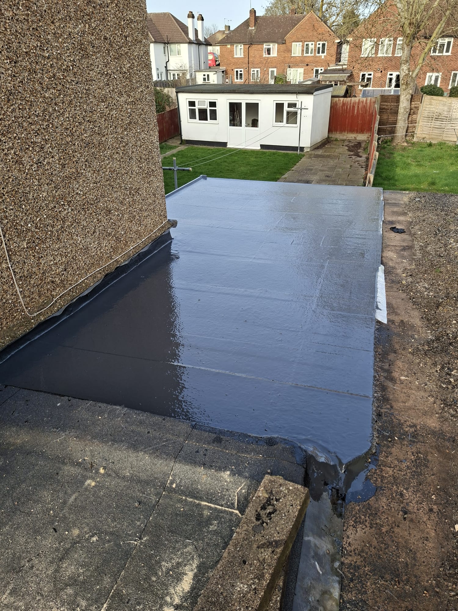 Completed rubber roof on extension with garden and fence in view
